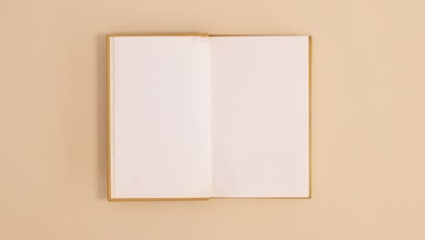 golden hardcover vintage book appear and open with copy space on beige background. stop motion flat lay