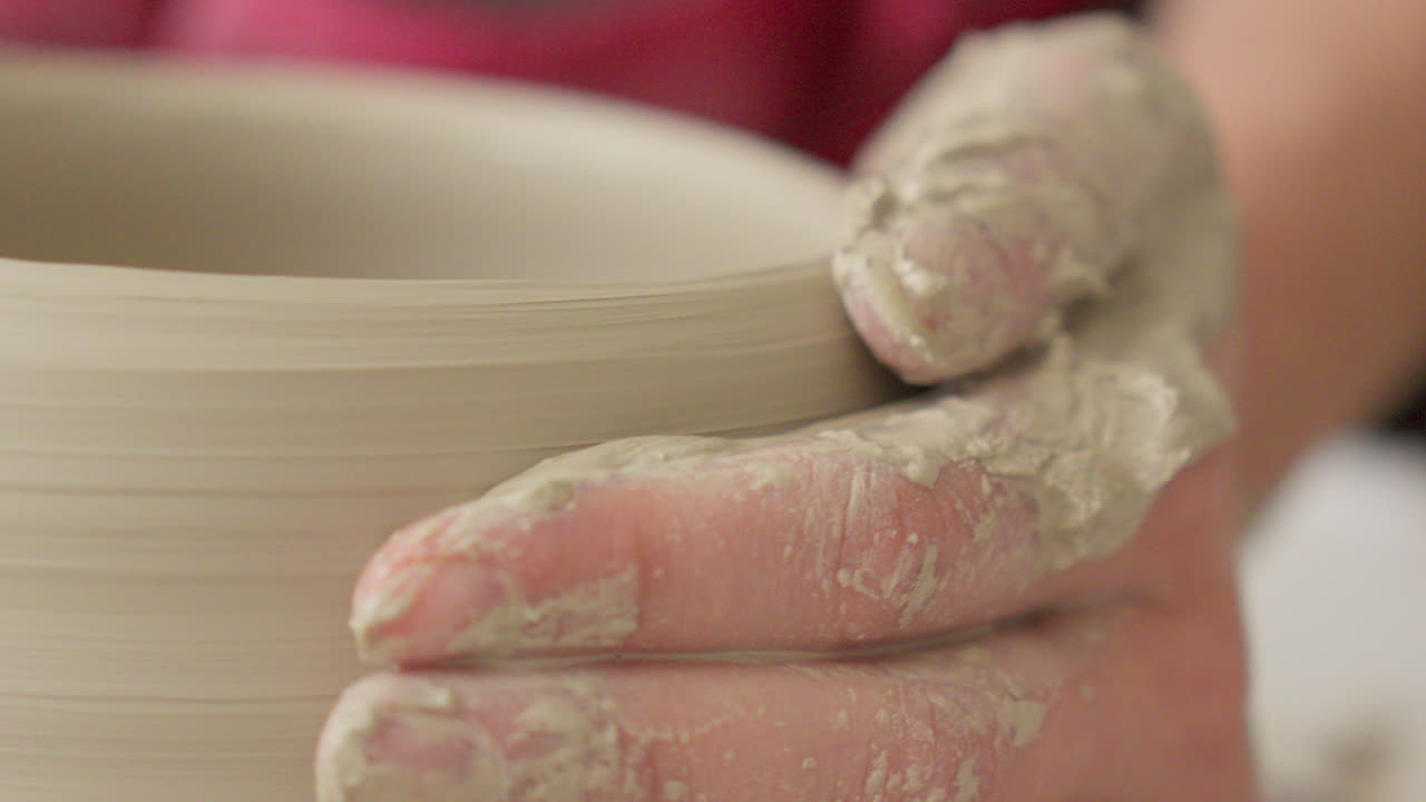 Pottery artist smoothing the walls of a bowl on a throwing wheel with both hands