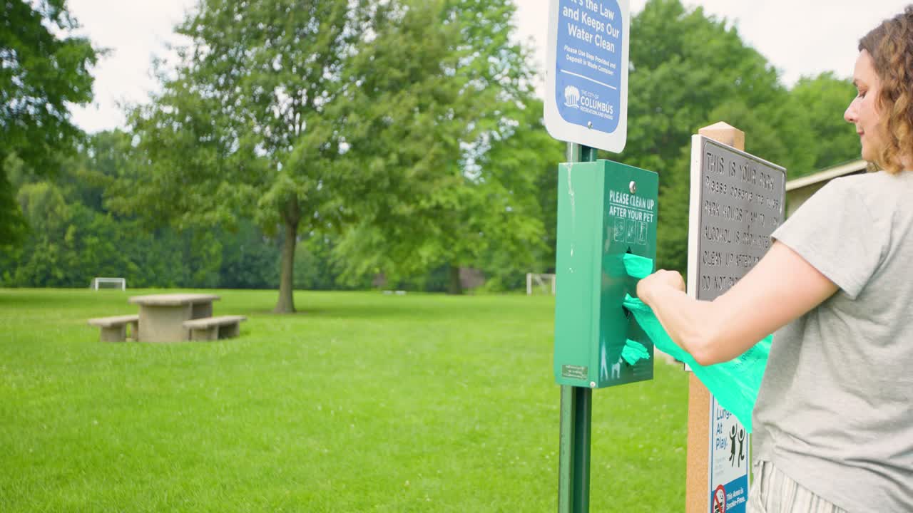 개 주인이 공원 쓰레기통에서 쓰레기봉투를 들고 개를 치운다
