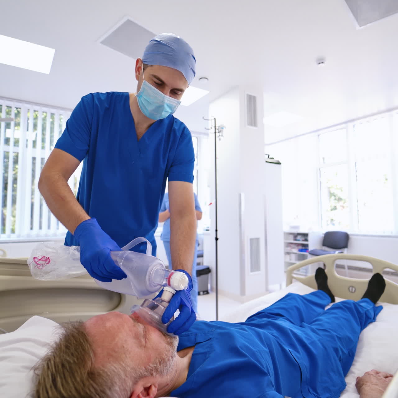 Professional doctor gives resuscitation to a male patient indoors. Doctor in mask and medical uniform helps a patient on the background of modern emergency room.