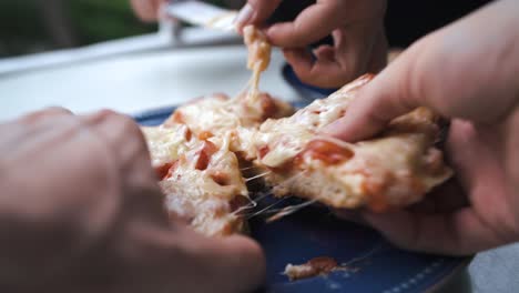 close up of hands taking homemade pizza slices with a lot of cheese on it