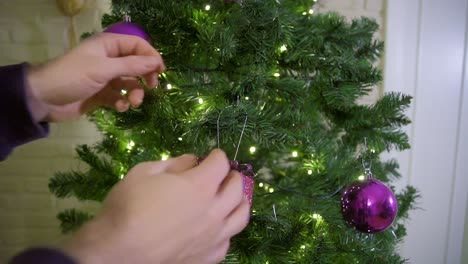 disparo estático de un adulto joven colgando decoración navideña en el árbol de navidad durante la temporada navideña