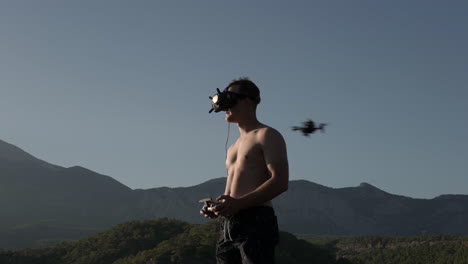 fpv drone flying by your man with goggles and remote controller with mountain hills in background