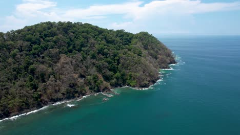 Herradura-Island-in-Costa-Rica,-covered-with-lush-green-forest-on-sunny-day--aerial