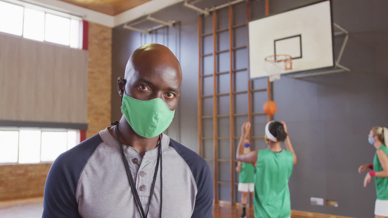Portrait of african american male coach with diverse female basketball team in background