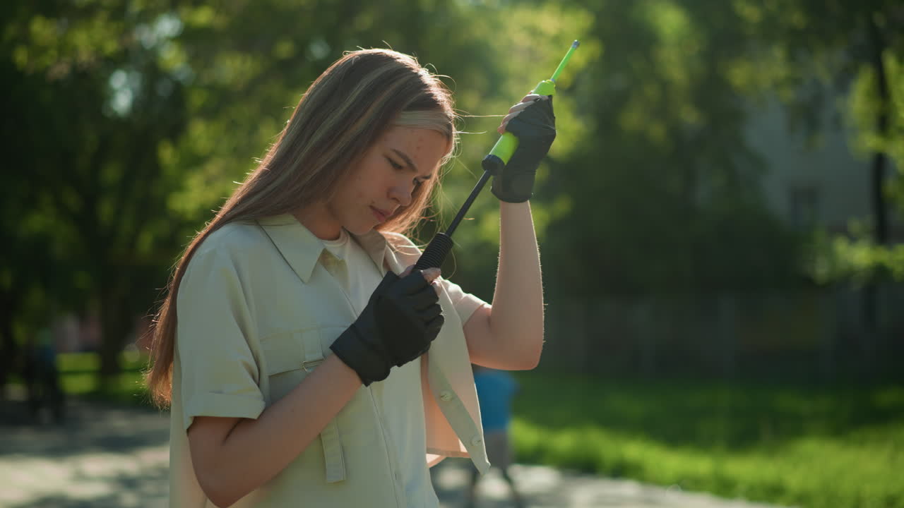 금발 머리카락을 가진 젊은 소녀는 야외에 서서, 사려 깊게 녹색 공기 프 손잡이를 조사, 파란 셔츠와 빨간 헬 롤러 스케이트 소년은 부드러운 초점