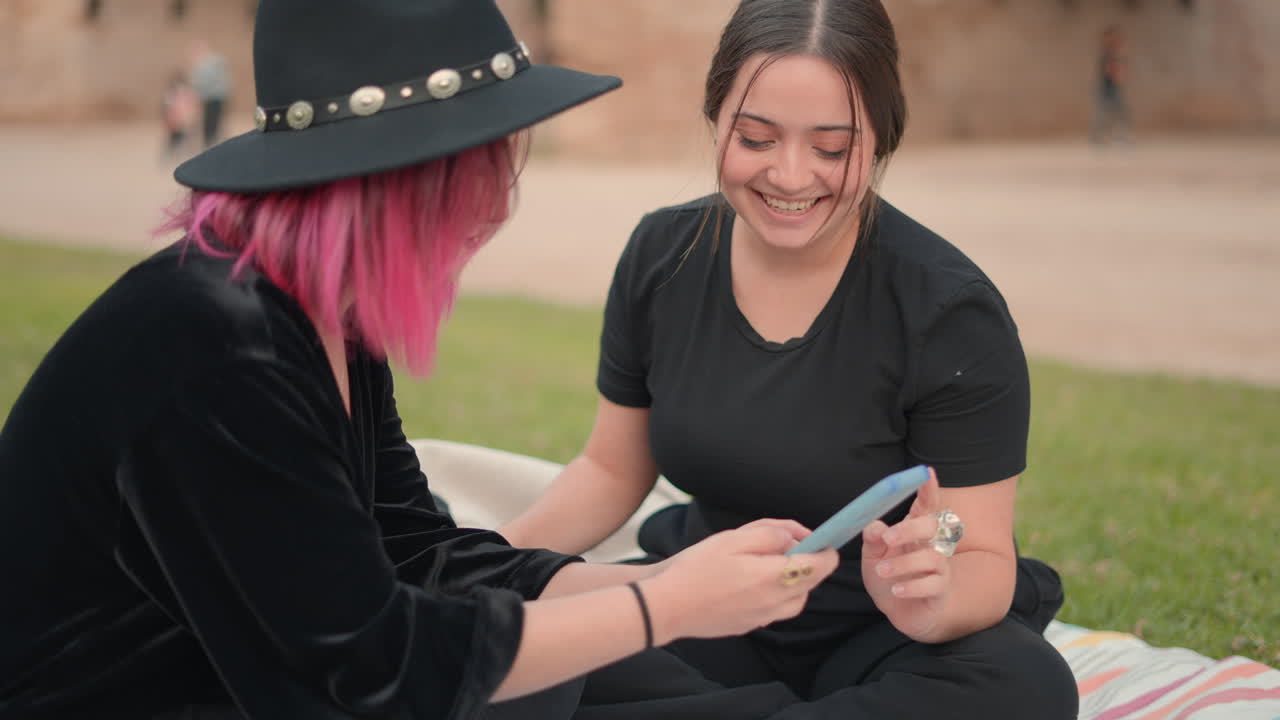 Two women laughing and looking at a phone in the park