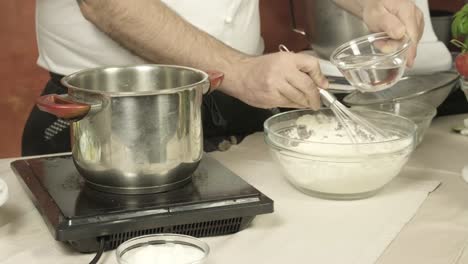 Cerrar-Las-Manos-Del-Chef-Italiano-Agregar-Agua-A-La-Harina-Blanca,-Freír-Masa-En-La-Cocina