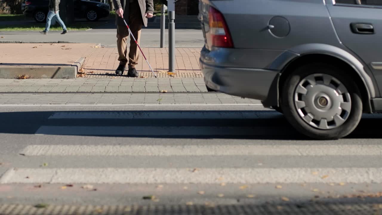 시각장애인 남자가 자신의 지이로 도로를 건너고 있는 모습이 도시에서 시각장애인을 위한 촉각적인 보행자 보행자 도로의 도움으로 보여진다.