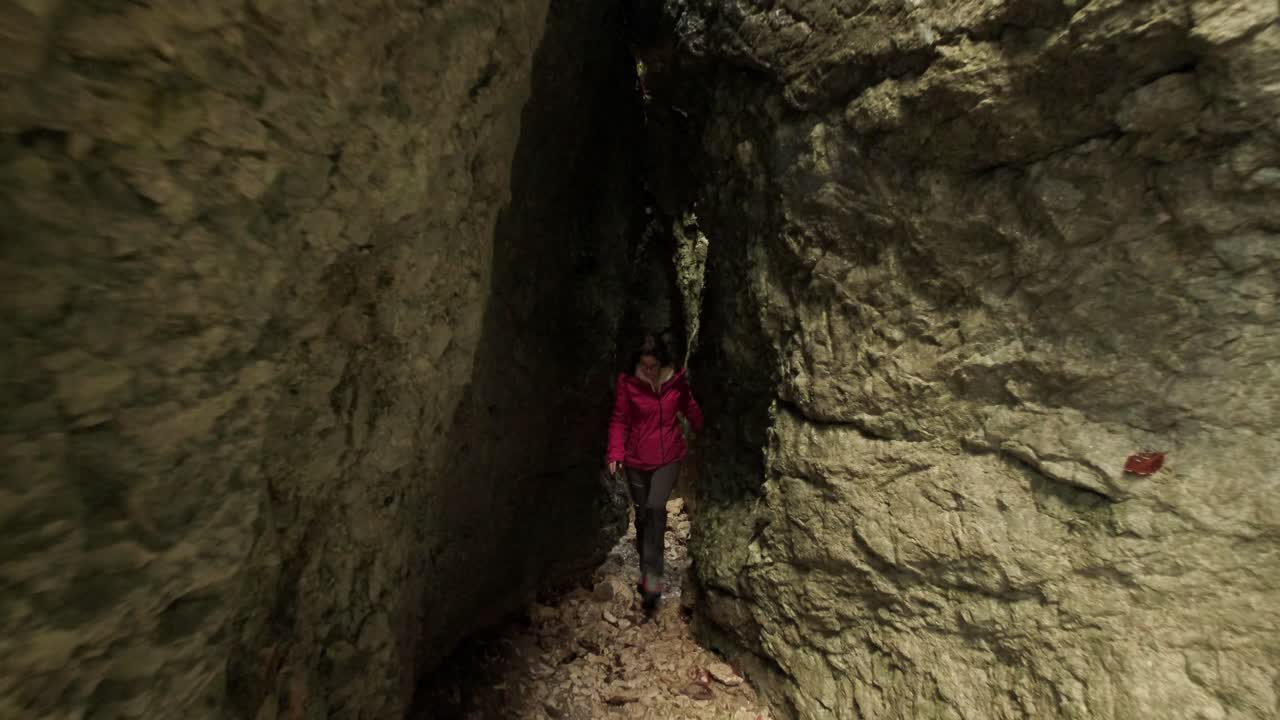 Lady wearing a pink jacket walking through a tight gorge towards the camera. The camera is panning back through the middle of the gorge. Pokljuka Gorge in Slovenia Triglav National Park