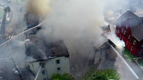 smoke fills the air in the aftermath of an apartment building fire with firefighters on site, panning drone shot