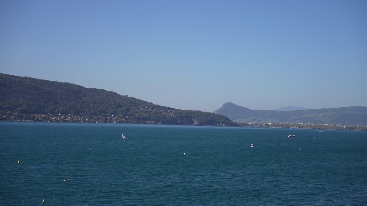 Sailboats on Lake Annecy in the French Alps on a sunny day, Wide pan right shot