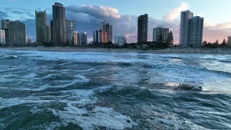 drone shot low over ocean, flying towards apartment towards, with waves and sun reflecting off water