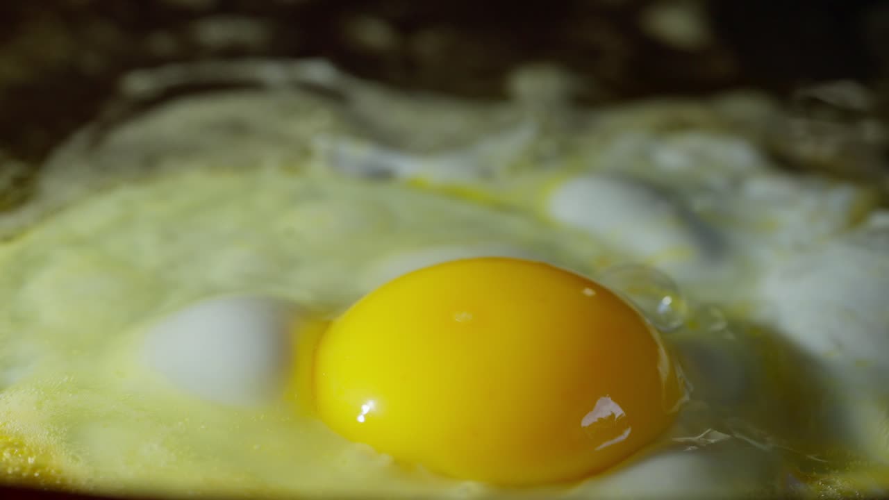 Fresh egg frying in sizzling butter on hot pan surface, macro slow motion view