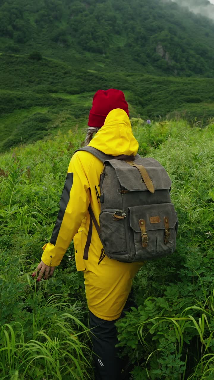 Escursionista con impermeabile giallo che cammina attraverso un rigoglioso paesaggio montano verde