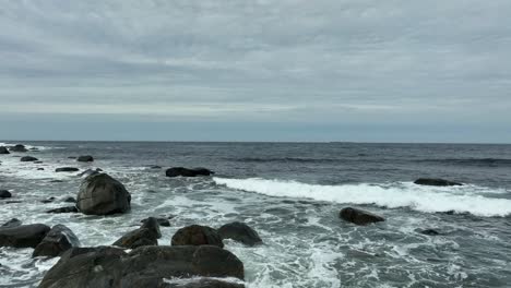 atlantic ocean waves crushing up on rocky shoreline in western norway - aerial close to surface at afternoon with cloudy sky