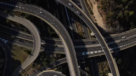 row of intersecting and intertwined roads with overpasses and smooth traffic in the early evening from a drone, looking down