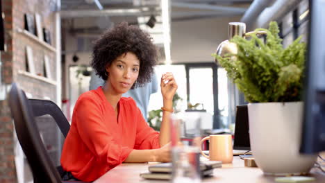 biracial woman in red blouse working at her desk in modern office