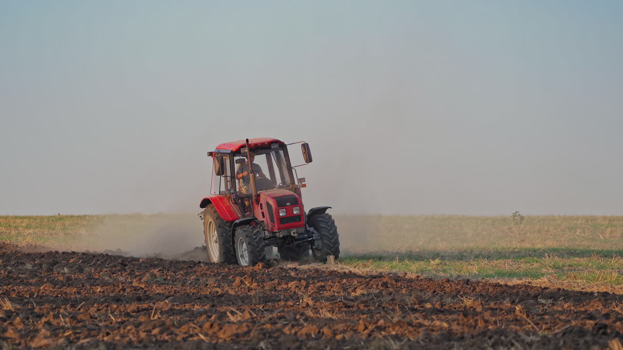 Red tractor at work. Agricultural machine plowing the field at daytime. Cultivation of land outdoors.