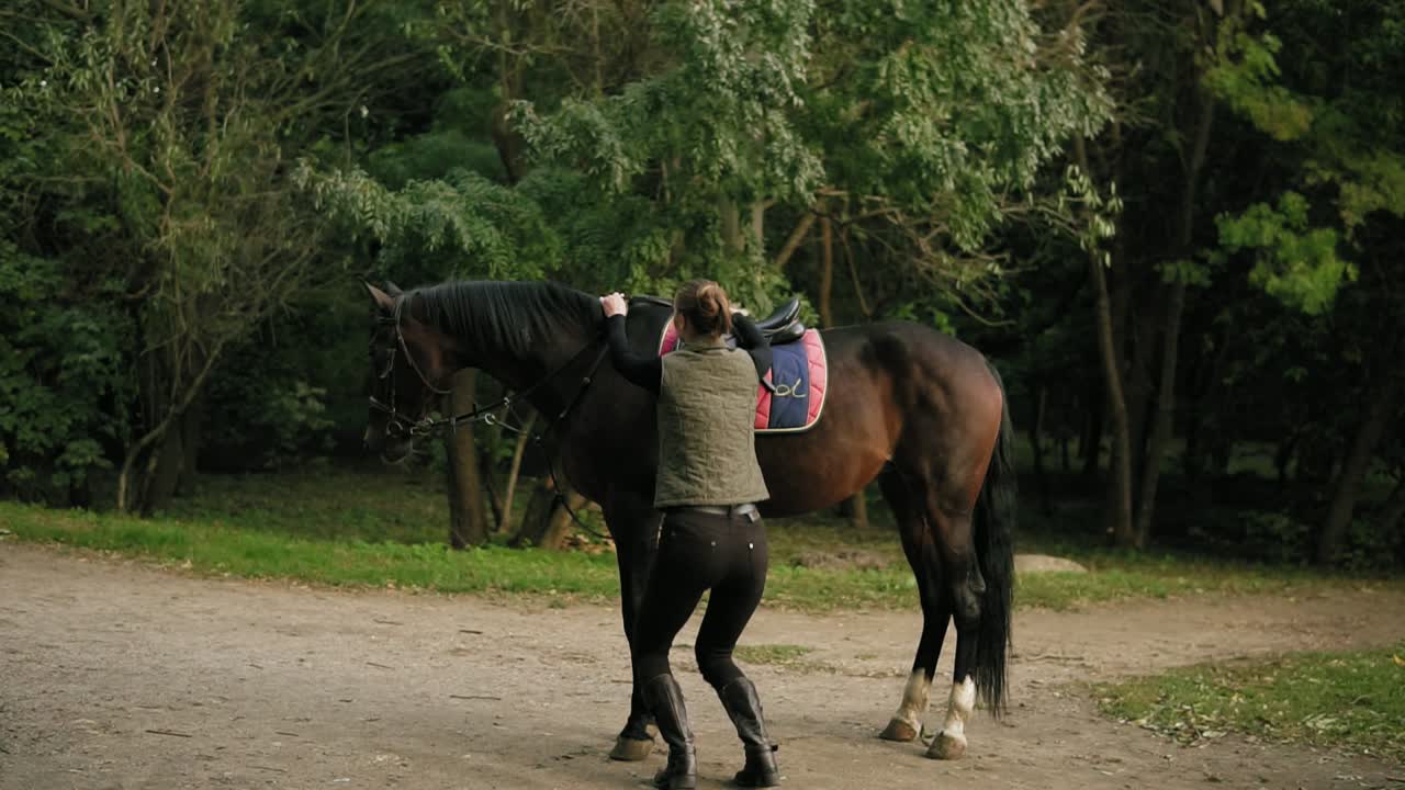 joven jinete profesional descendiendo del caballo, saltando al suelo, mirando a la cámara y sonriendo