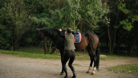 young female professional horse rider dismounting from the horse, jumping on the ground, looking in the camera and smiling