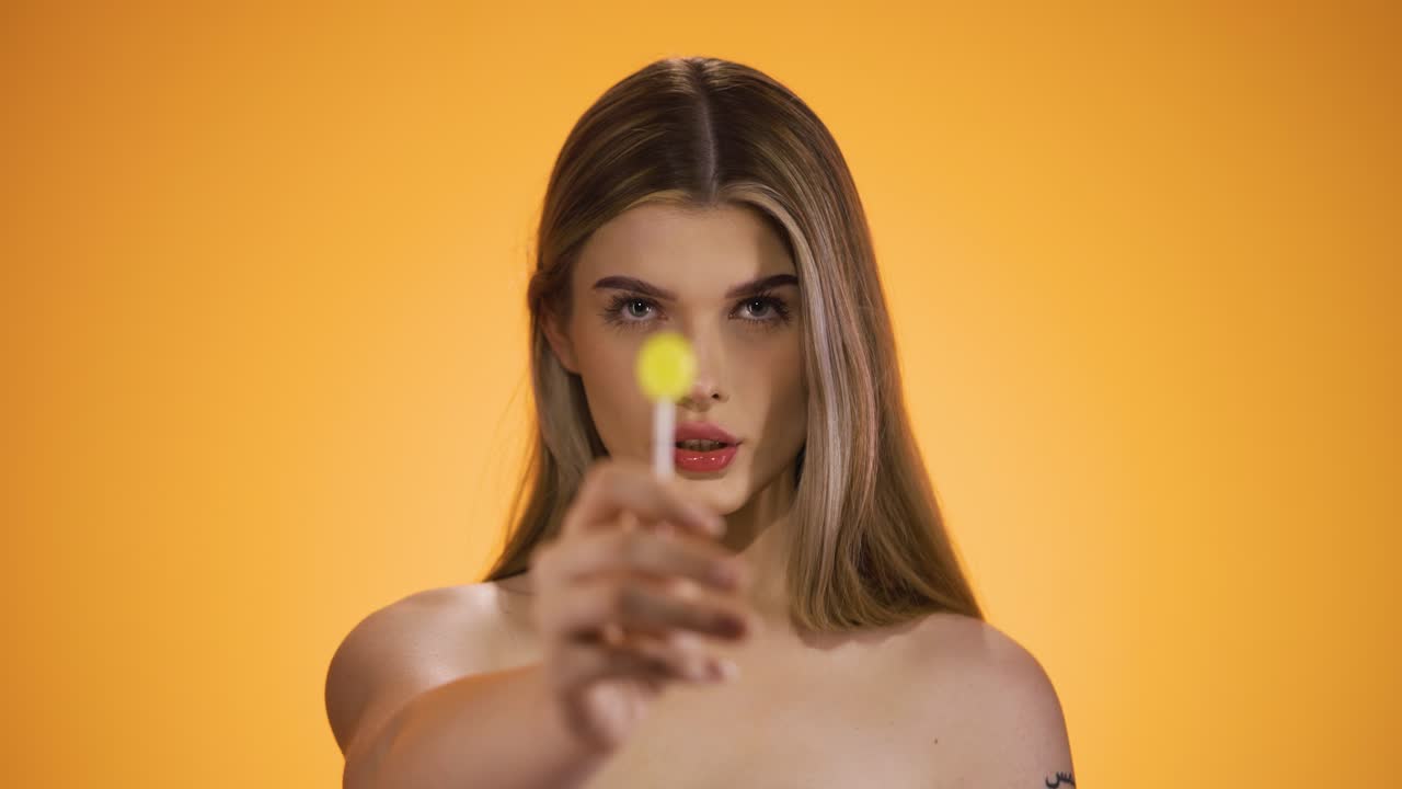 Static medium shot of a Seductive Blonde Young Caucasian Woman Licks a delicious sweet Lollipop and enjoy the candy against Chroma Background Staring with Naked Torso