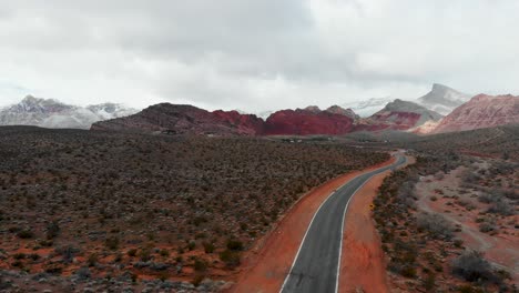 Aerial-drone-shot-along-an-empty-road-with-snow-flurries-and-mountains-in-the-background