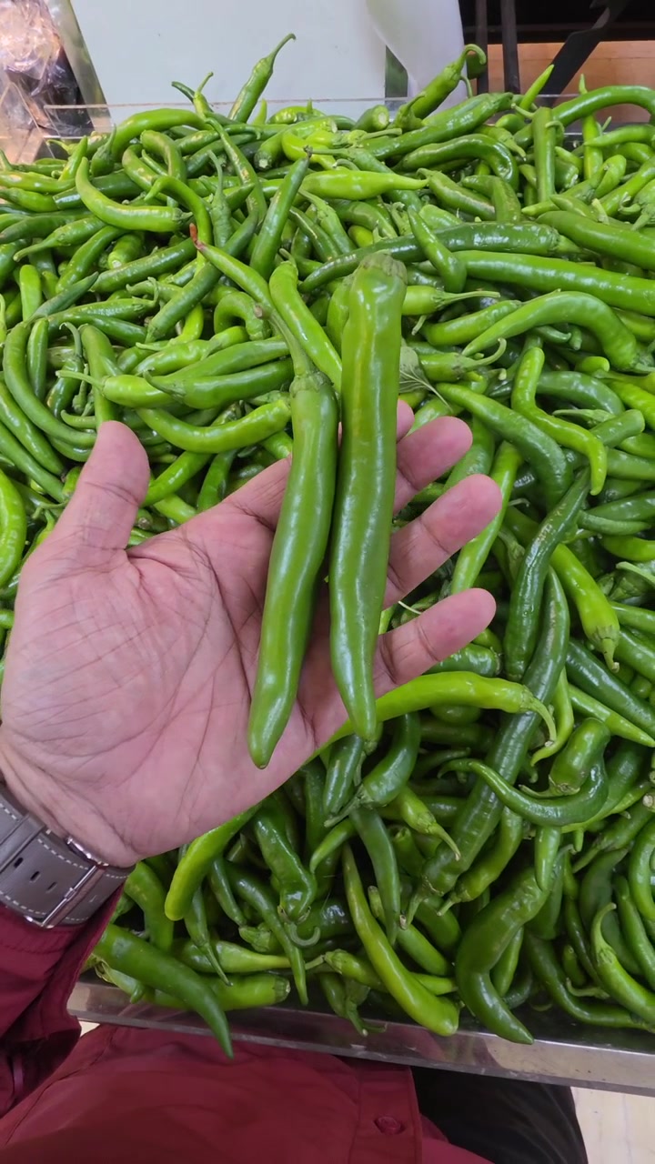 A hand holding green chillies while shopping in a supermarket