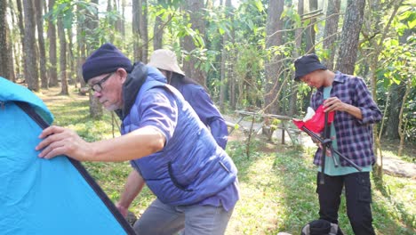 elderly asian father with two teenager kids setting up tent for camping in nature in summer