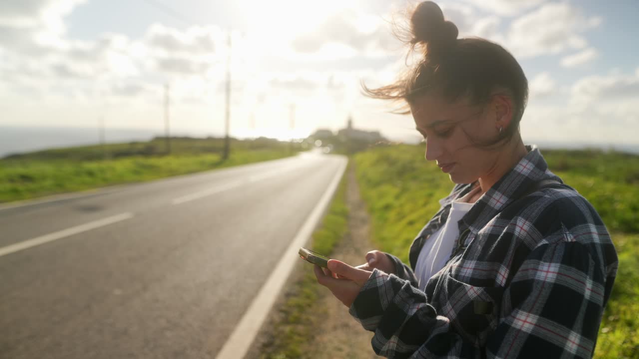 adolescente usando el teléfono al lado de la carretera en un día soleado