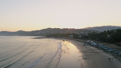 Antena-De-Puesta-De-Sol-En-Una-Playa-Tranquila-Con-Siluetas-De-Personas-Y-Pájaros-Volando,-4k