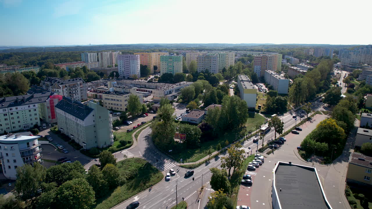A drone shot of a vibrant residential area with traffic on a main street in Witomino, Gdynia, Poland, under a clear blue sky on a sunny day