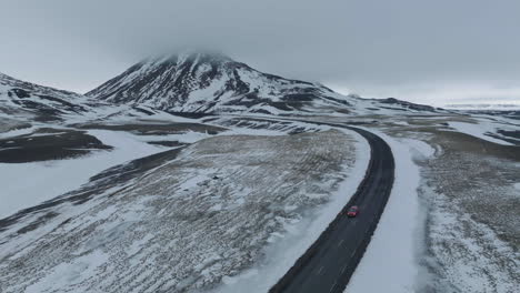 aerial view of red car on wet icelandic ring road and snow capped volcanic hills