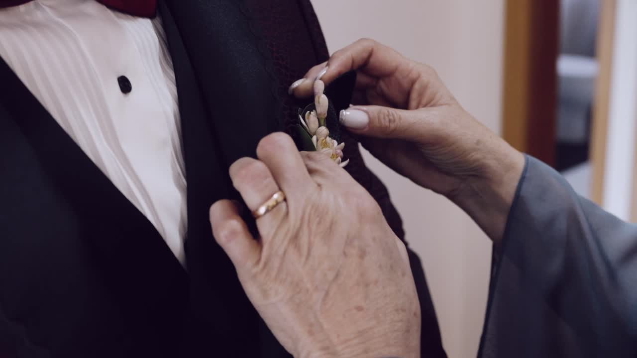 Close up of a mother pinning a boutonniere on her son's tuxedo for his wedding