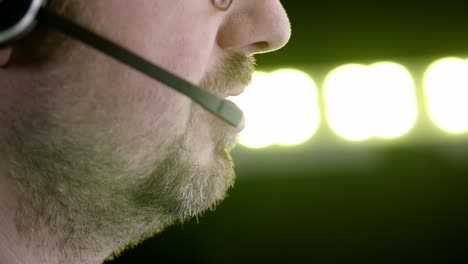 Close-up-man-speaks-into-headset,-background-lights-cycle-thru-colours