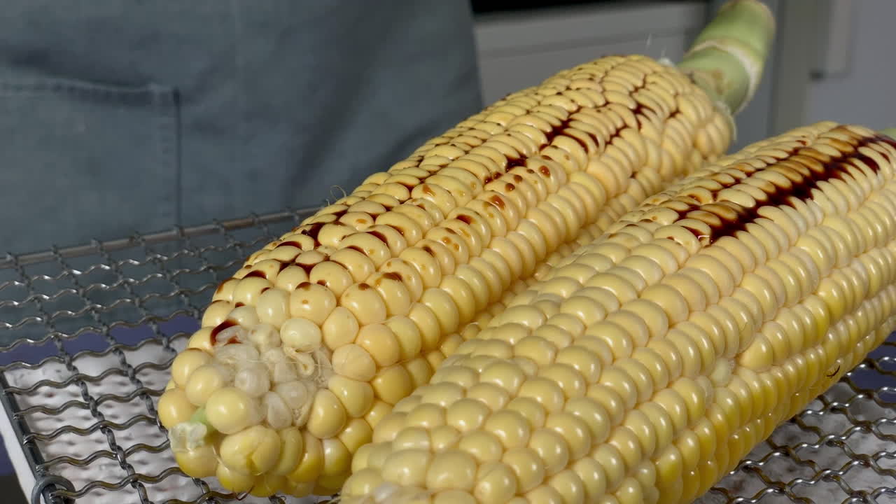 una chef japonesa pone shoyu en maíz a la parrilla en la cocina de su casa, tokio, japón