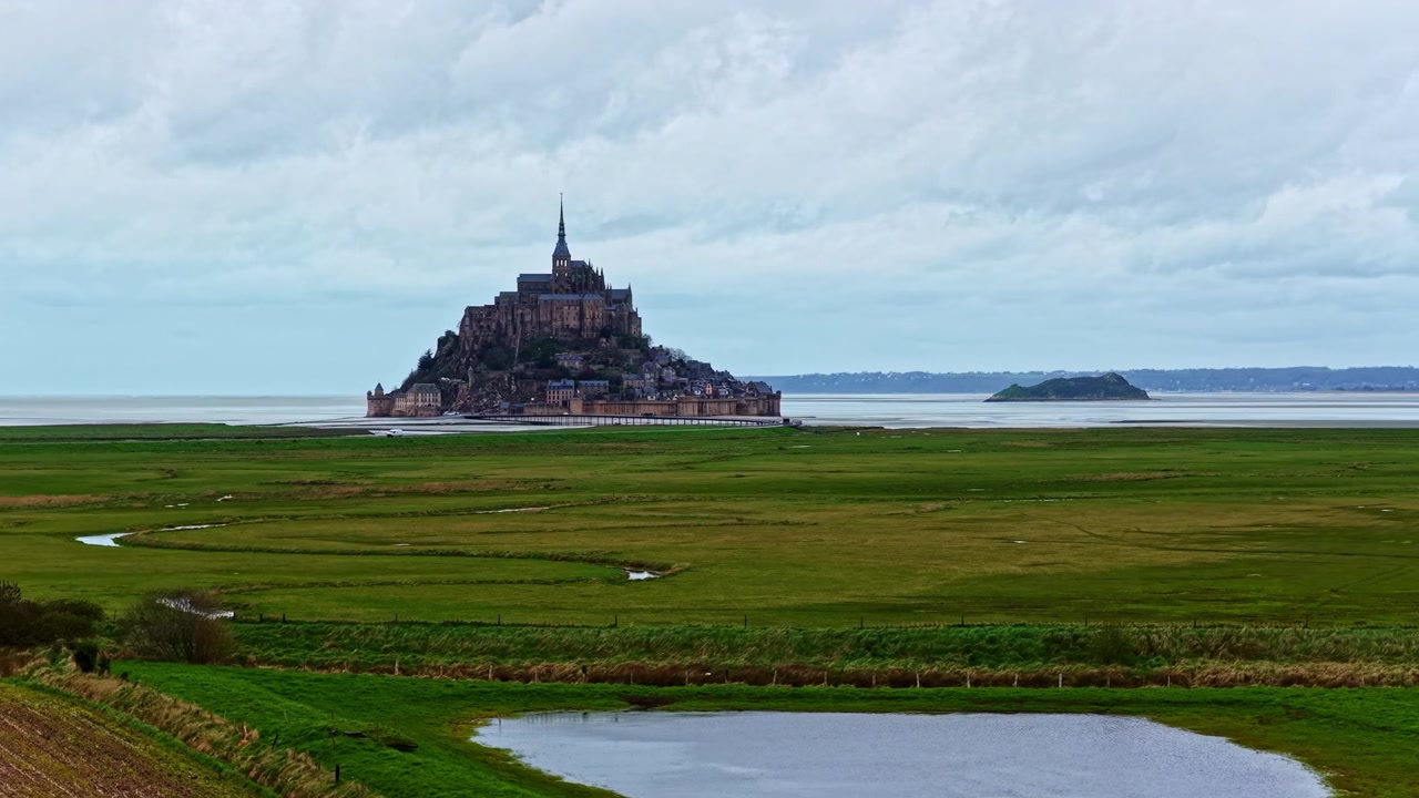 Le Mont Saint-Michel se dresse majestueusement sur un vaste arrière-plan côtier, entouré de riches pâturages verdoyants. Idéal pour les documentaires historiques et les reportages de voyage.