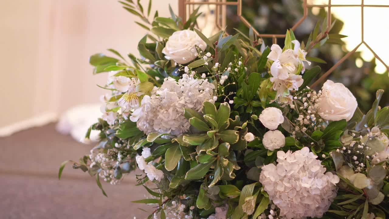 Tavolo principale di un ricevimento di matrimonio con bellissimi fiori freschi, rose bianche, foglie di eucalipto e altro fogliame verde.