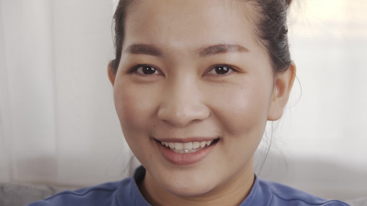 미소와 함께 소파에 앉아 파란색 셔츠를 입고 아시아 여자는 행복하게 휴식