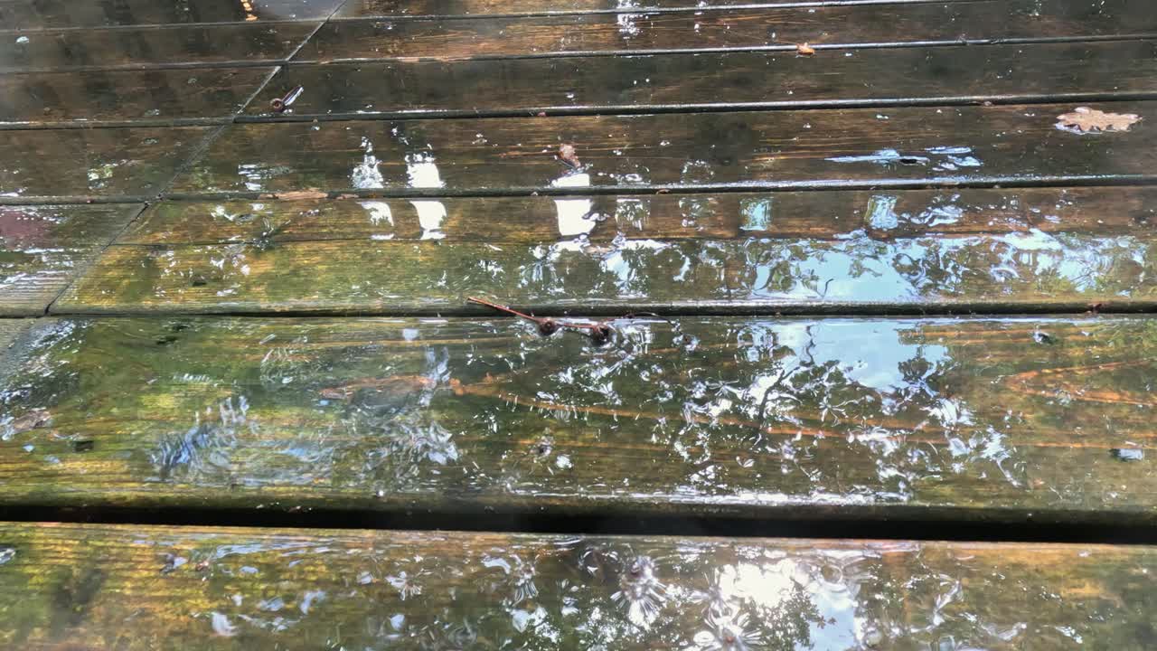 Rain water drips onto wet wooden deck outside, close-up detail view