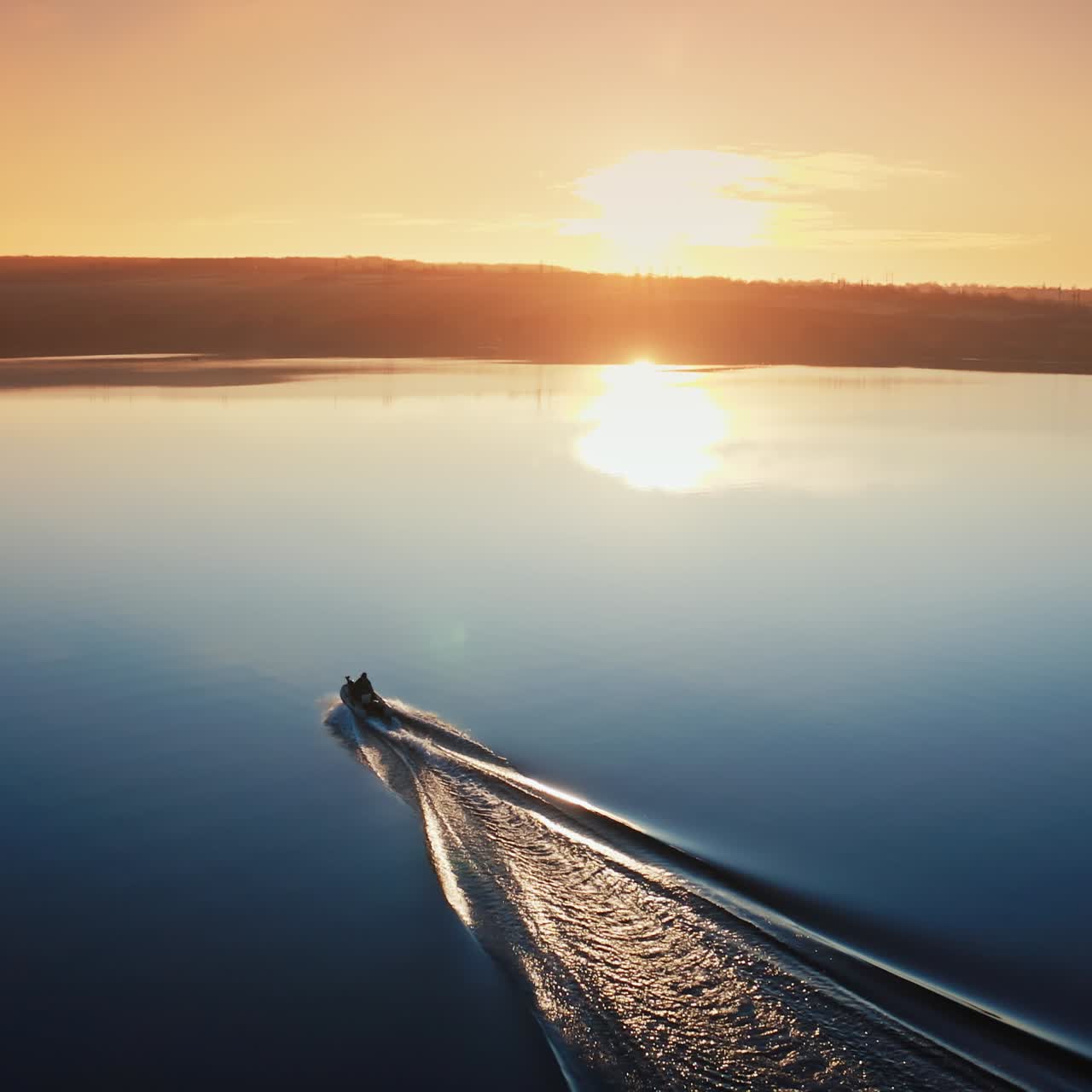 Aerial view of a motor boat at sunset. Calm water in a blue lake in the evening. People in a boat moving along the river.