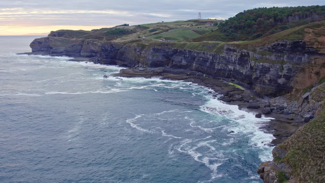 Drone capture the aerial shot of island of Isla with waves of Cantabrian sea hitting the shore at the sunset