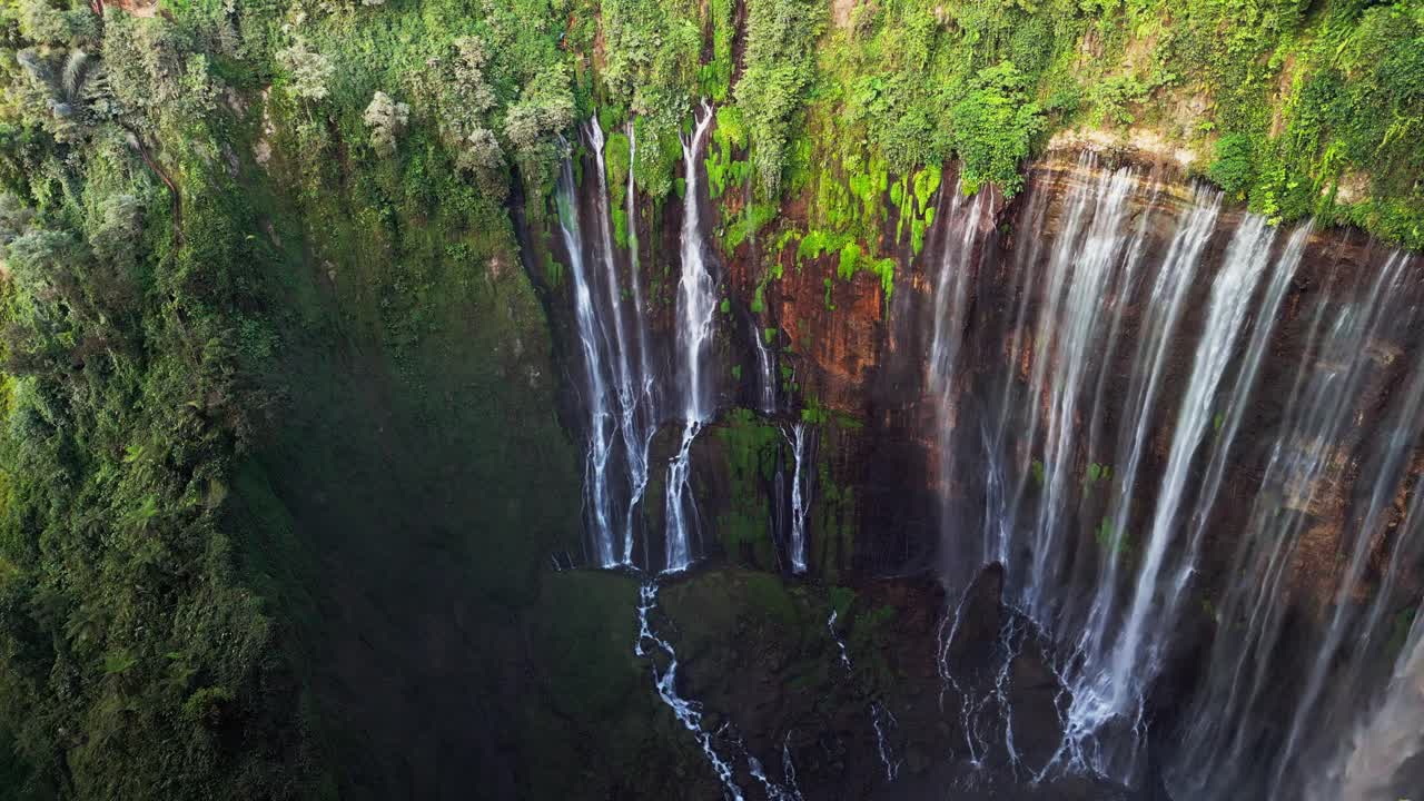 Rekaman stok dari udara yang menampilkan air terjun bertingkat Tumpak Sewu di Indonesia saat beberapa aliran menuruni jurang kapur yang dalam dengan aliran sungai yang terlihat mengalirkan kabut dan medan tropis yang terjal