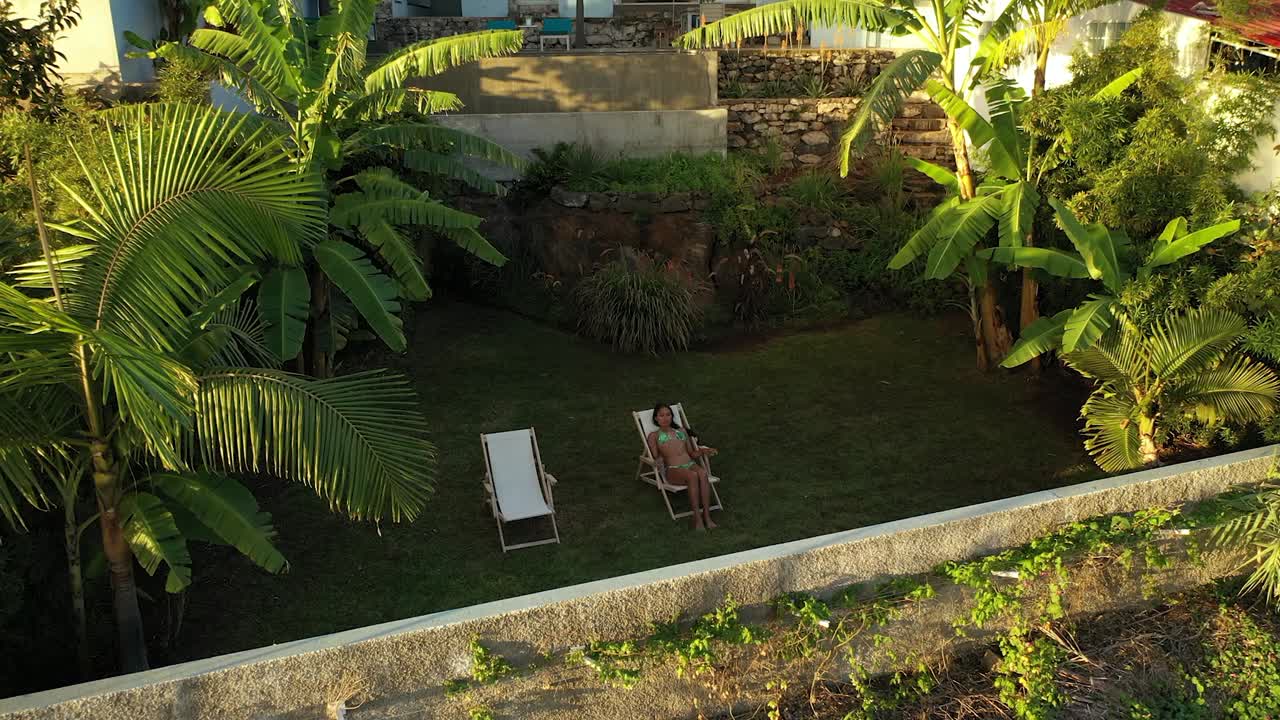 A young and beautiful woman is sitting or laying down in the sunchair in a bikini