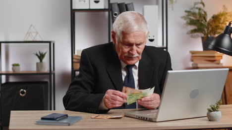 rich senior businessman working on laptop counting money cash calculate earnings at home office
