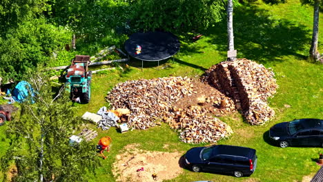 aerial view of a countryside yard with tractor, stacked firewood, trampoline and parked cars in summer