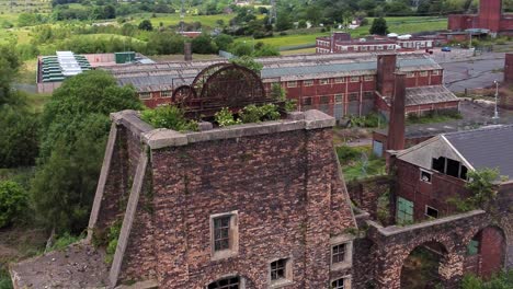 Abandoned-old-overgrown-coal-mine-industrial-rusting-pit-wheel-aerial-view-orbit-right-close-rising