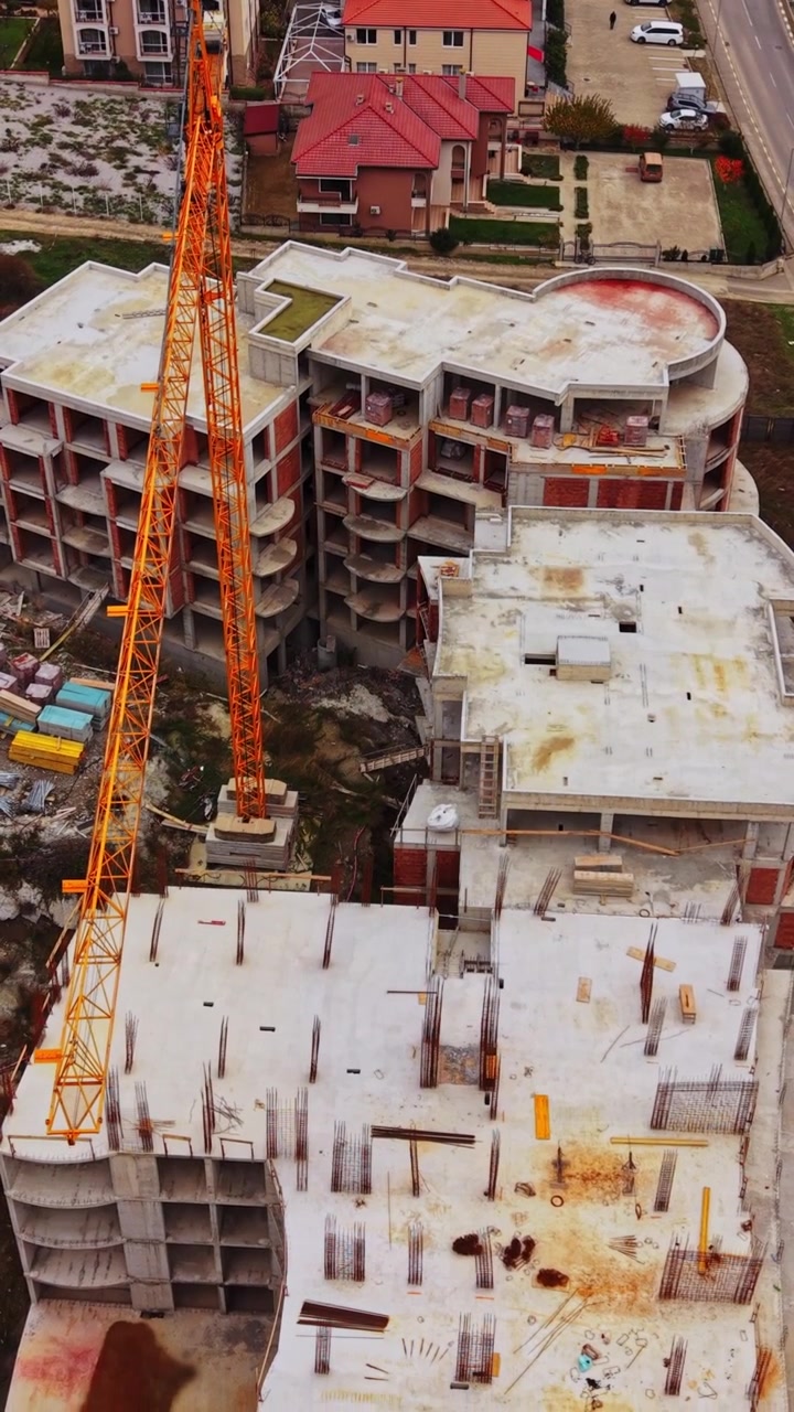 Obra en construcción con una grúa y edificios cercanos en vista aérea