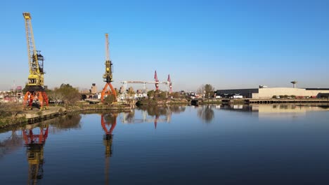 4k aerial drone footage of container cranes along clear calm waters in buenos aires la boca, argentina with blue skies