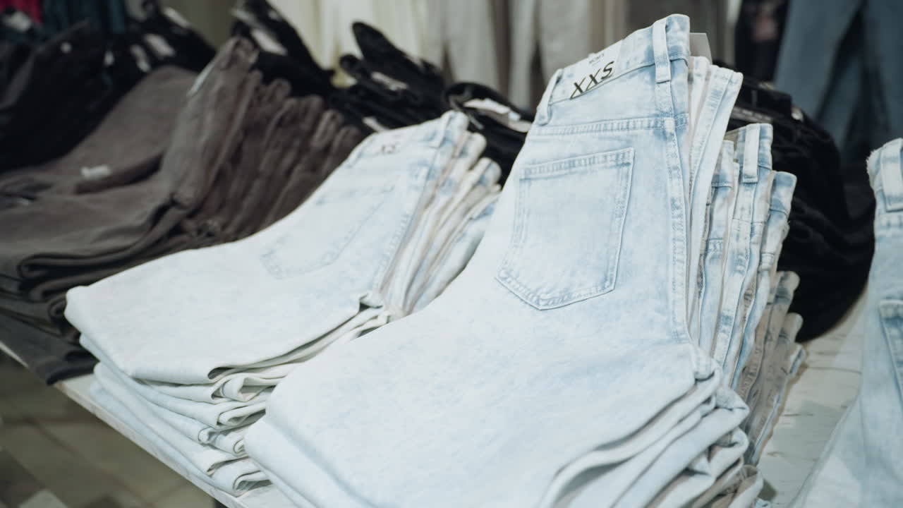 vista en primera persona de una tienda de ropa con vaqueros bien plegados en varios tonos, organizados en estantes de exhibición. arreglo ordenado y variedad de denim disponibles en un entorno minorista moderno